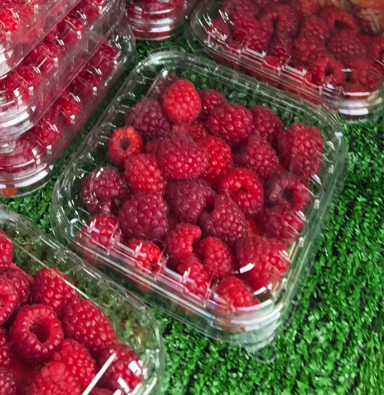 plastic punnets of raspberries on a green-covered table